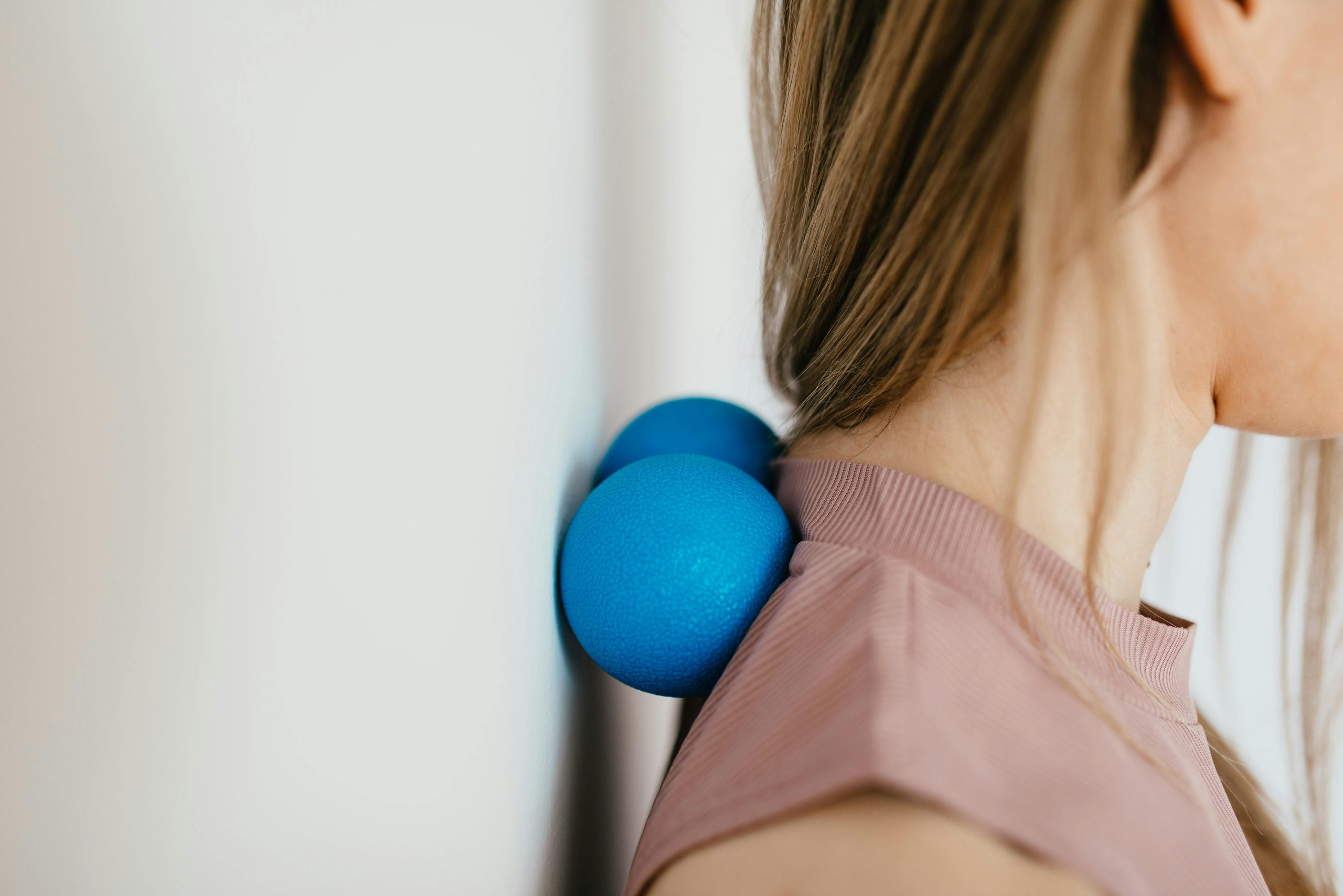 pexels-photo-4498297-4498297 Close-up of woman using blue massage balls for neck relief against a wall.