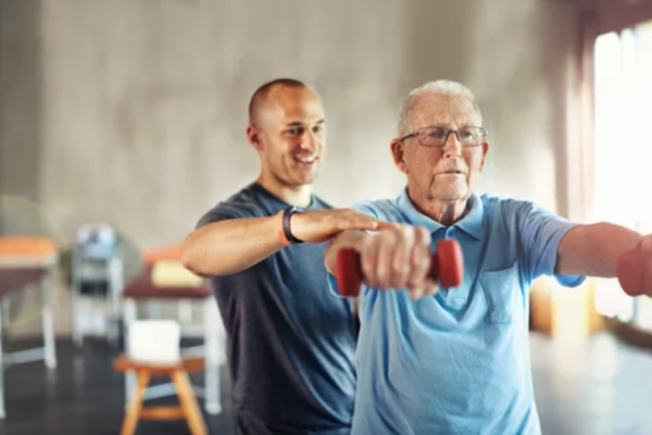 Elderly man exercising with dumbbells alongside his physical therapist