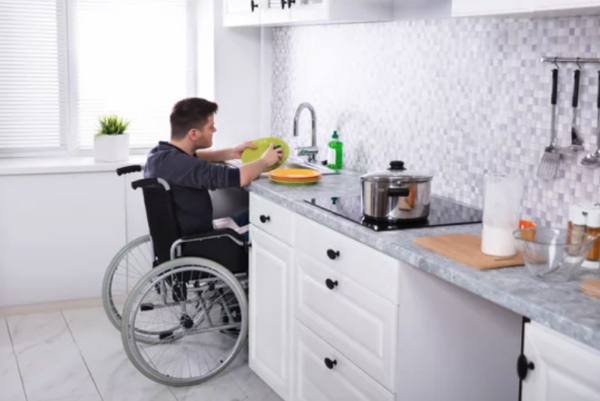Man in a wheelchair reaching for dishes in an accessible kitchen